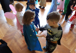 Dzieci tańczą. Na pierwszym planie dziewczynka w niebieskiej pelerynie i chłopiec przebrany za Batmana.